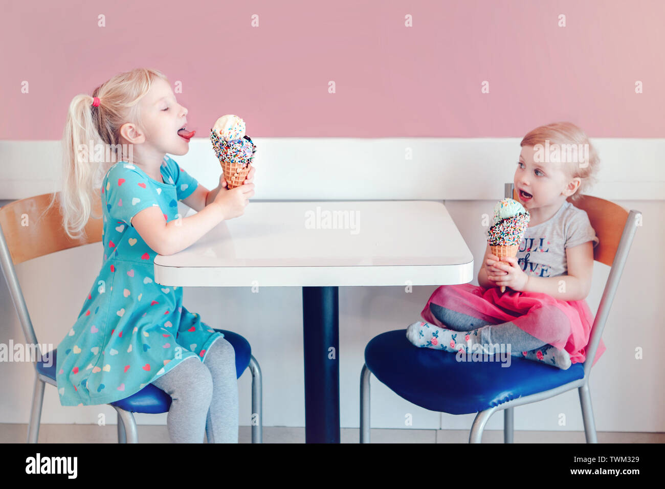 Stile di vita ritratto di due felice Caucasian carino adorabili bambini divertenti ragazze seduti insieme a mangiare leccare il gelato con colorati spruzza. Amore e Foto Stock