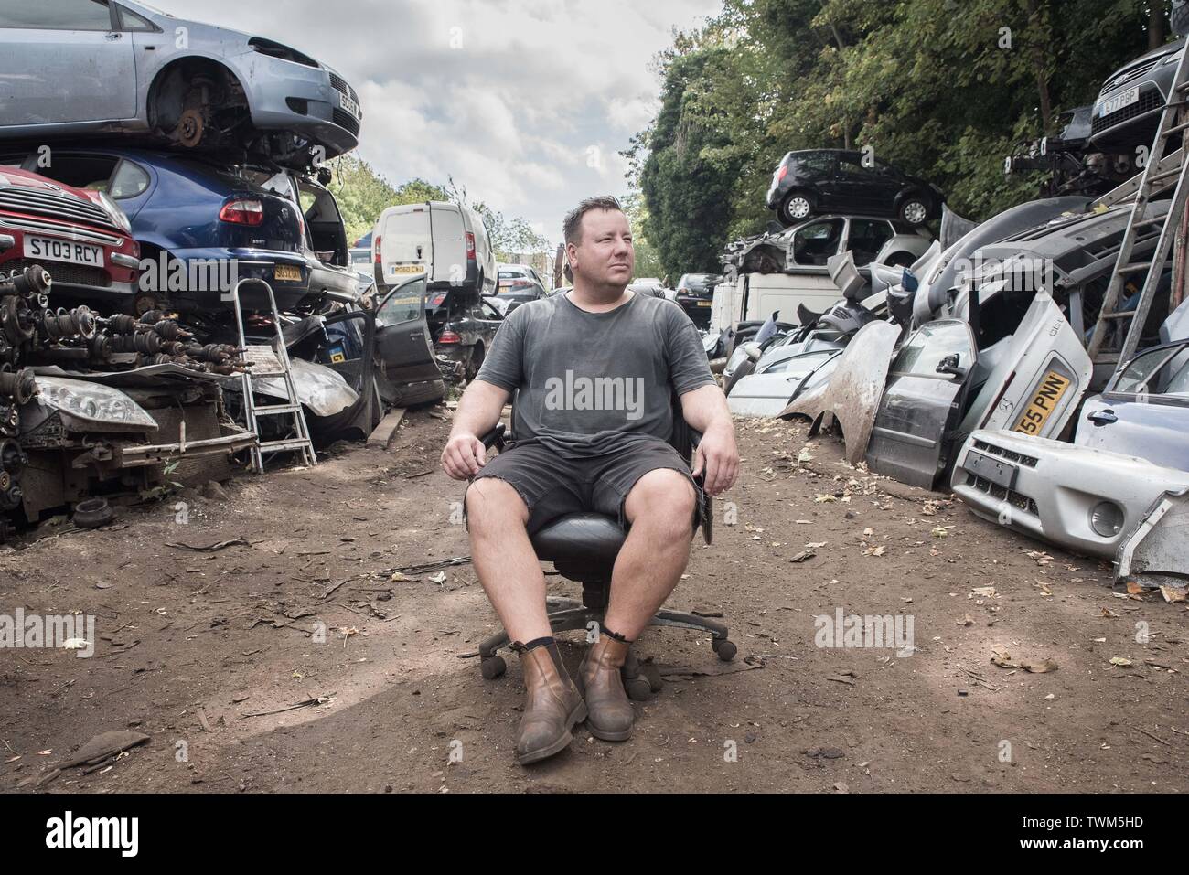 Demolitori auto cantiere proprietario di affari si siede orgogliosamente nella sua sedia per ufficio nel cantiere Foto Stock