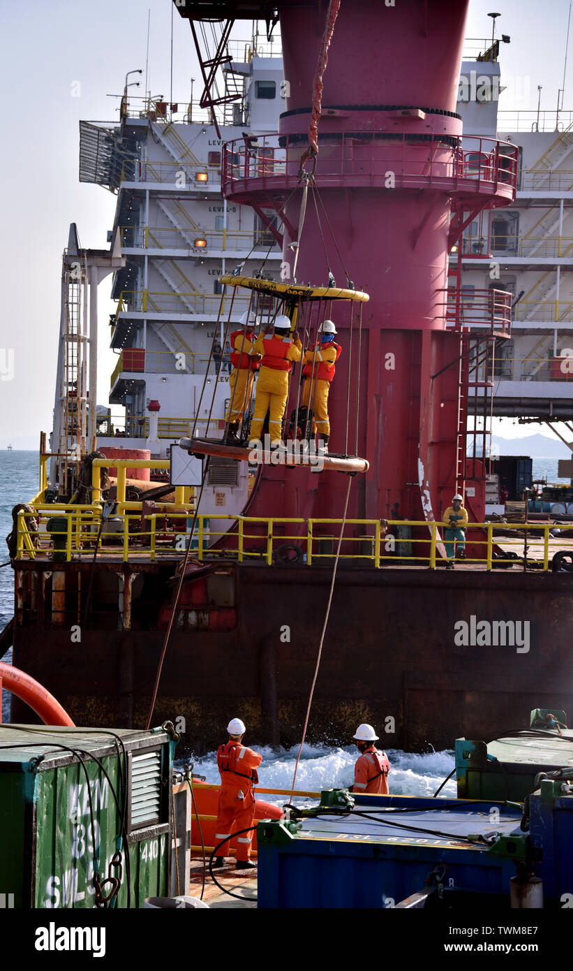 Equipaggio marino trasferisce olio piattaforma personale da alloggio barge al recipiente mediante gru Foto Stock