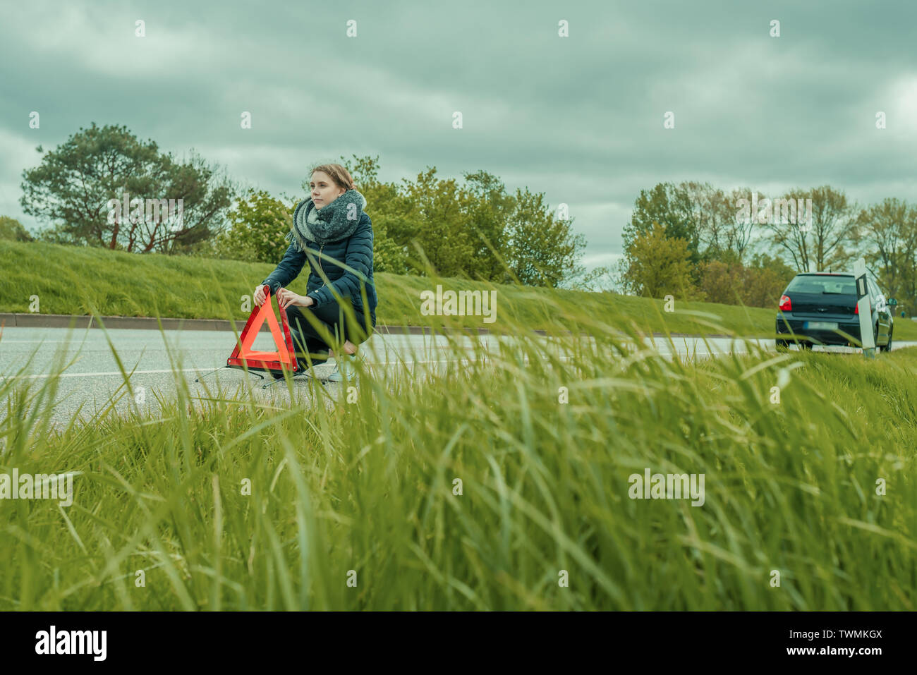Una giovane donna si mette in ginocchio e solleva il suo triangolo di avvertimento Foto Stock