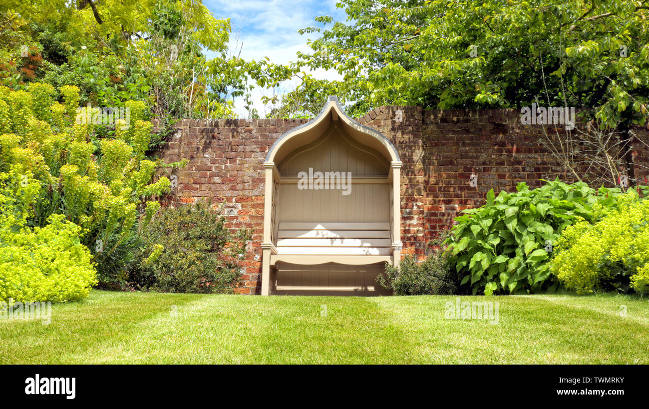 Vintage appartata panca in legno da un muro di mattoni, in un elegante giardino paesaggistico, in una giornata di sole in un paesaggio inglese . Foto Stock