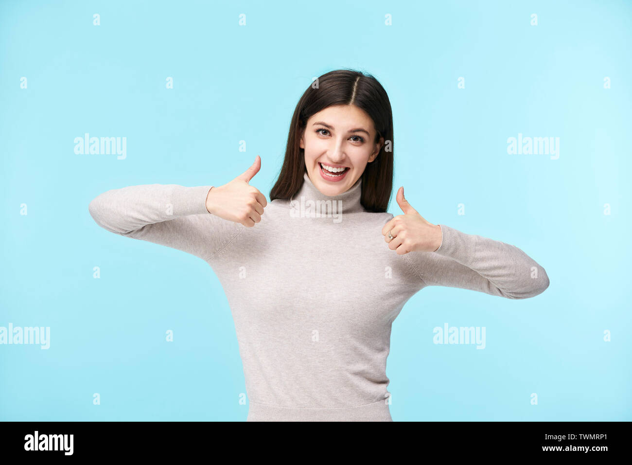 Ritratto di una giovane e bella donna caucasica con due dita verso l'alto, guardando la telecamera sorridendo, isolato su sfondo blu Foto Stock