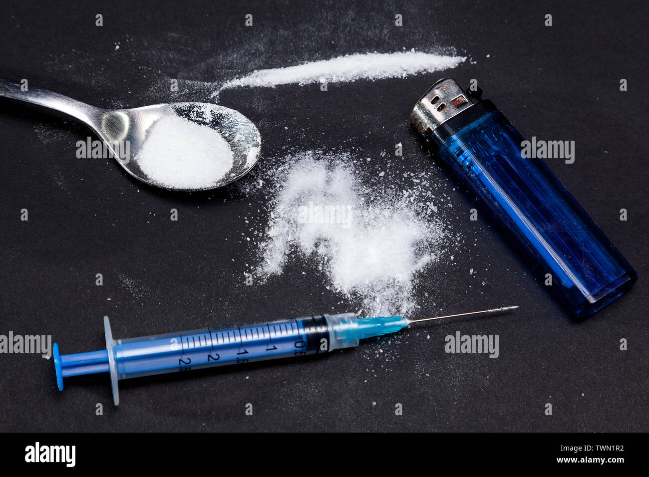 La cocaina in polvere in un cucchiaio e una siringa con farmaci su uno sfondo nero. Percorso di cocaina Foto Stock