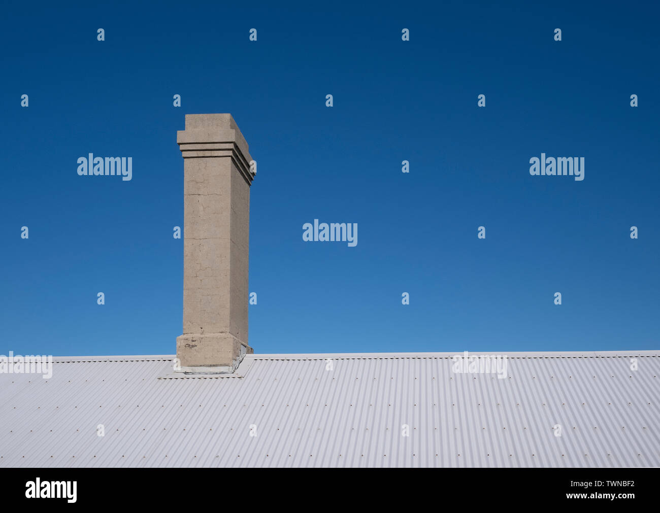 Il vecchio camino sul ferro corrugato tetto contro un cielo blu chiaro Foto Stock