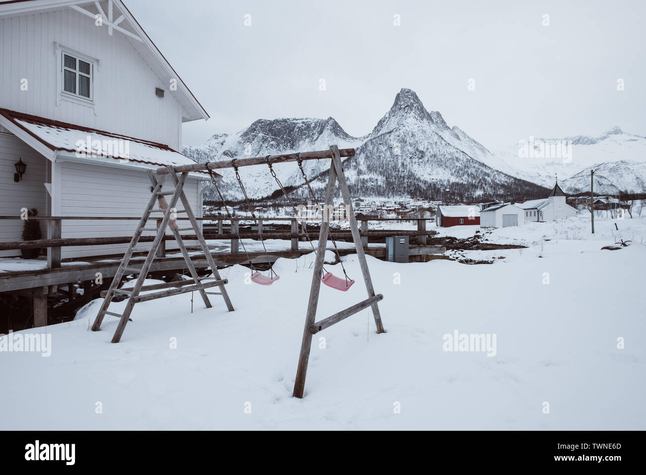 Altalene in legno che soffia sul parco giochi con la montagna innevata nella cortina di nubi Foto Stock