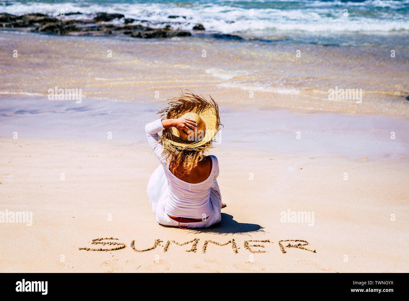 La gente di viaggio e in estate in spiaggia concetto all'aperto - casa vacanze le attività per il tempo libero - donna con cappello e abito bianco visto dalla parte posteriore di sedersi o Foto Stock