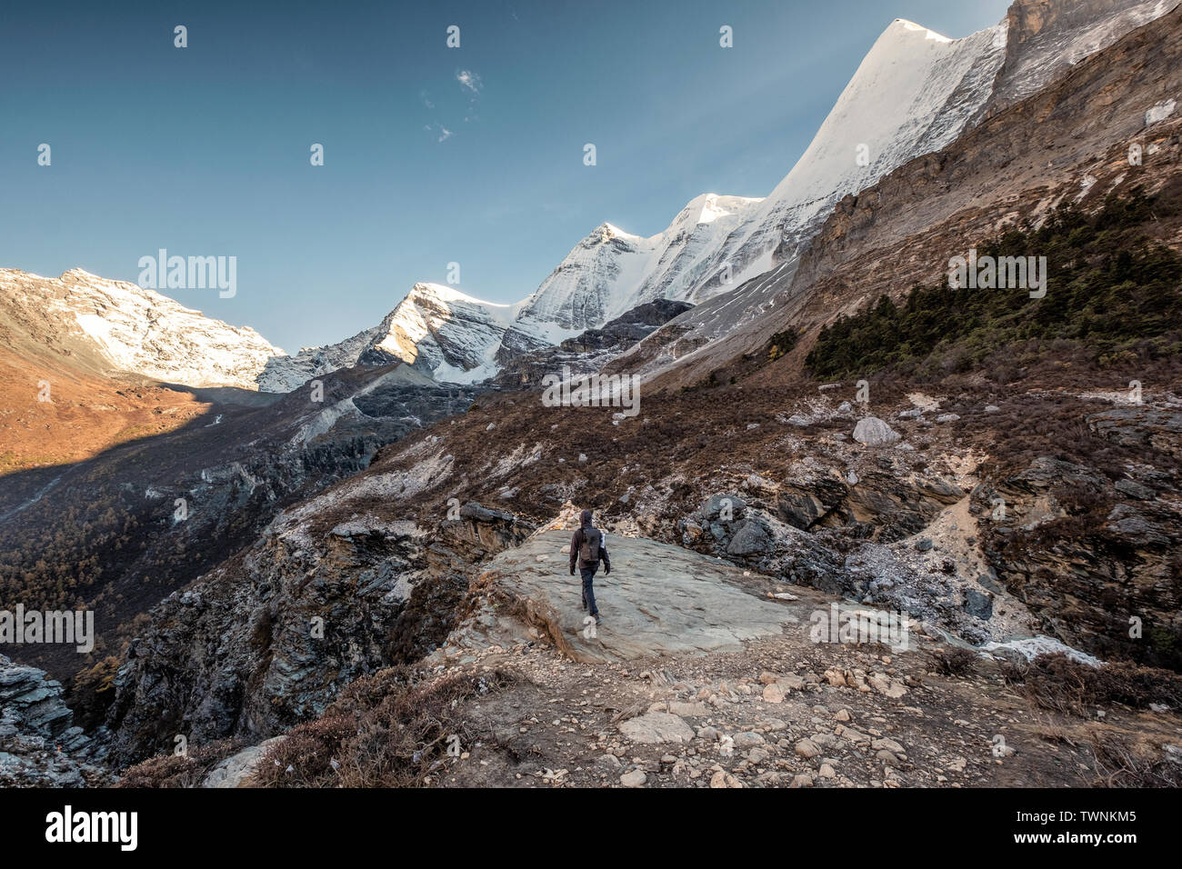 Uomo a piedi backpacker alla scogliera con neve montagna sullo sfondo di gamma Foto Stock