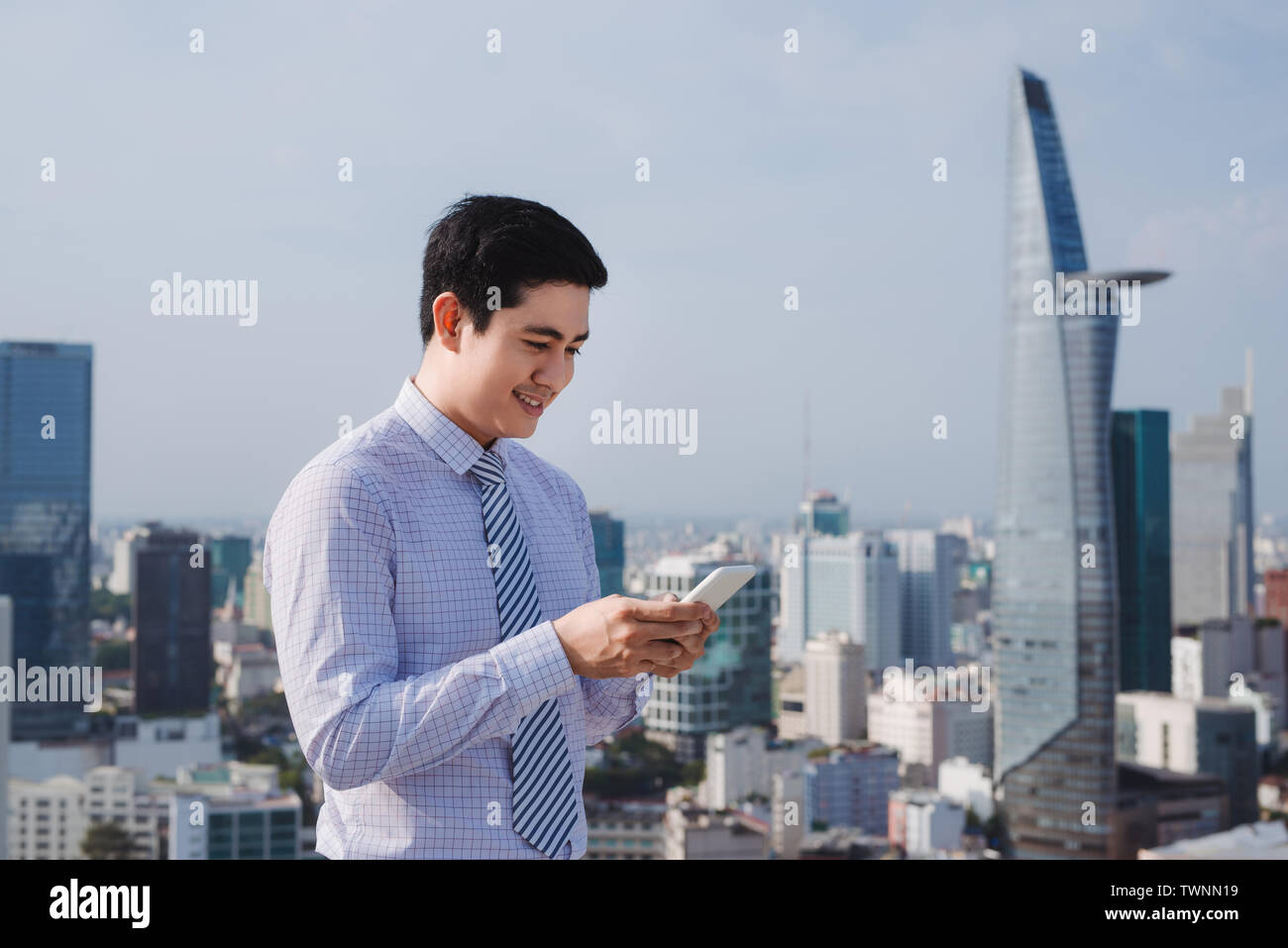 Imprenditore tramite telefono mobile app texting al di fuori dell'ufficio in città urbana con grattacieli edifici in background. Giovane uomo caucasico holding s Foto Stock