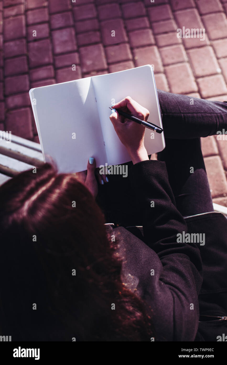 Bruna ragazza che lavora sui suoi compiti saggio o la ricerca di carta e di scrivere i suoi pensieri in un notebook che tiene nelle sue mani. Pav Foto Stock