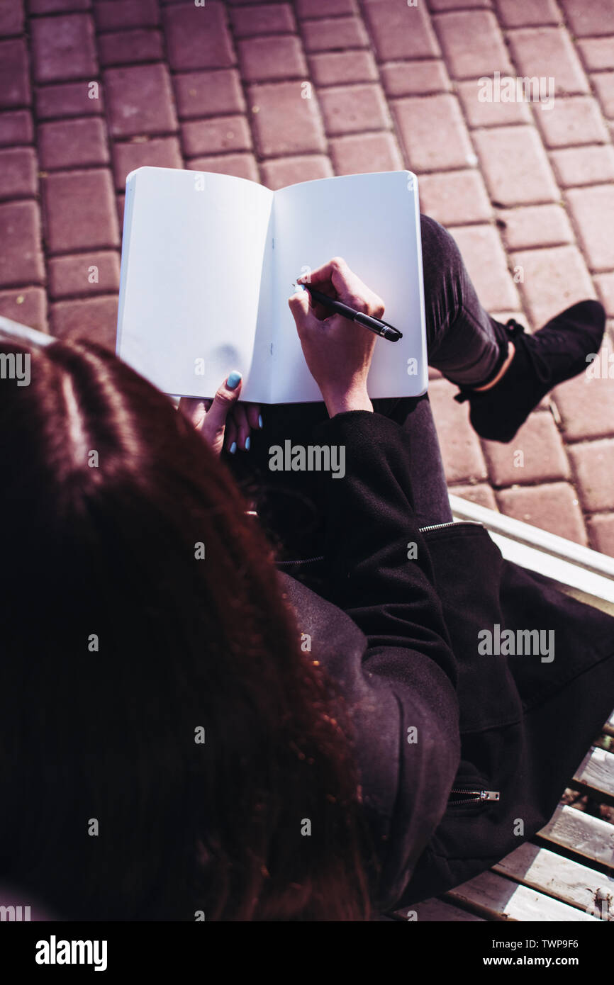 Bruna ragazza che lavora sui suoi compiti saggio o la ricerca di carta e di scrivere i suoi pensieri in un notebook che tiene nelle sue mani. Loo Foto Stock