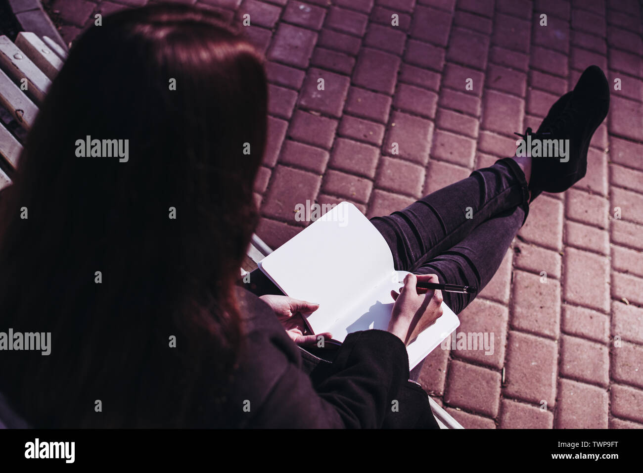 Bruna ragazza che lavora sui suoi compiti saggio o la ricerca di carta e di scrivere i suoi pensieri in un notebook. Marciapiede pavimentato su uno sfondo Foto Stock