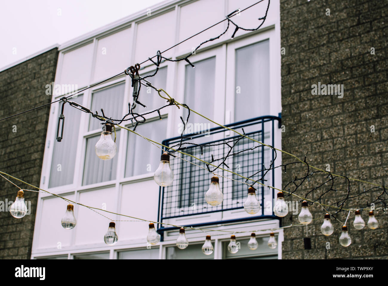 Vecchie lampadine usate piene d'acqua piovosa e appese su una scossa contro le pareti bianche e il balcone di un edificio in mattoni. Tranquillo quartiere di Haarlem Foto Stock