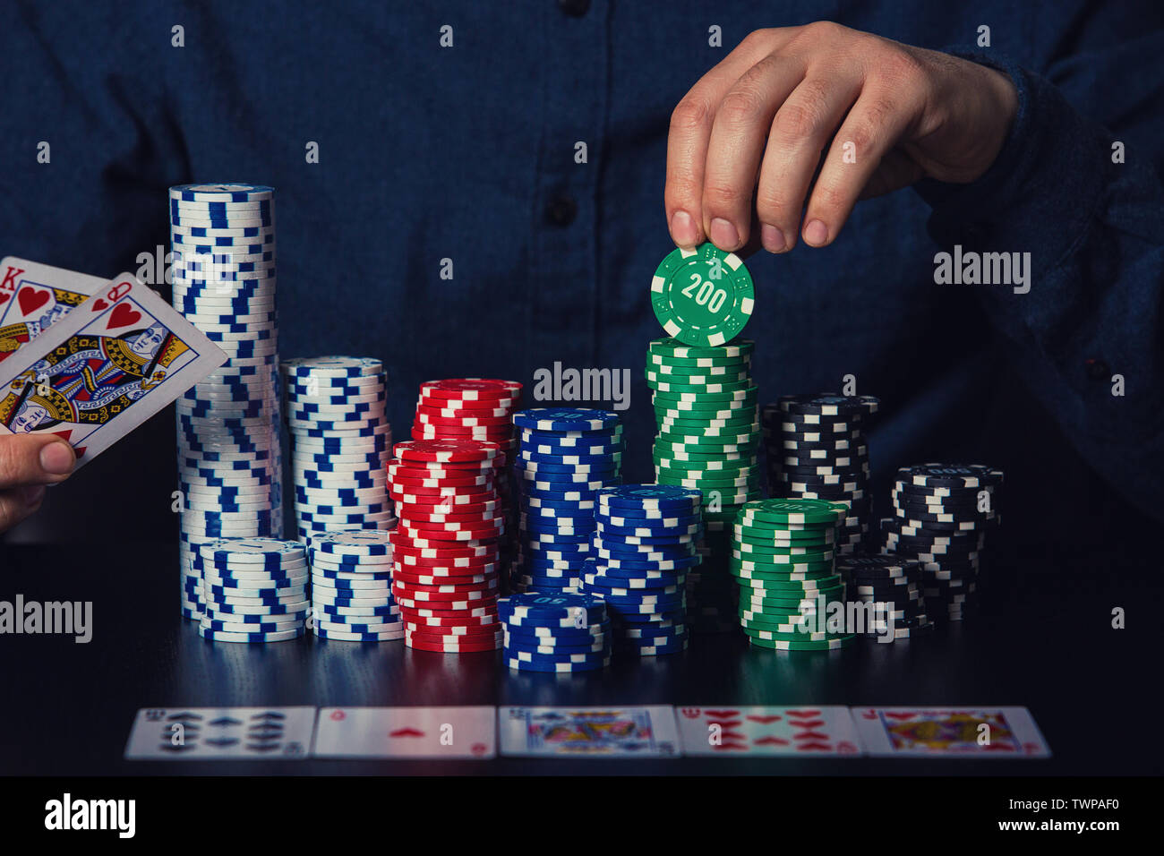 Chiusura del giovane giocatore di poker mani che mostra le schede e prendere chips al tavolo del casinò. Il gioco d'azzardo vincitore torneo concetto di successo oltre il buio torna Foto Stock
