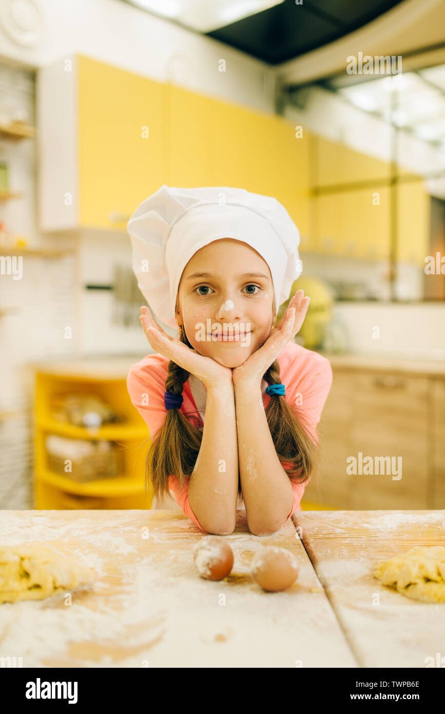 Bambina cuocere nel cappuccio e grembiule in cucina Foto Stock