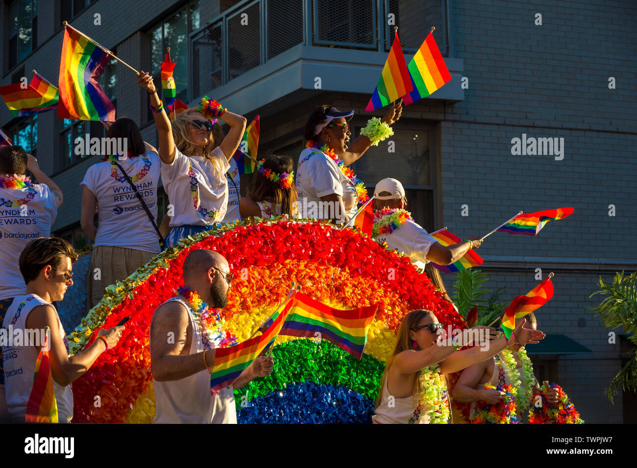 NEW YORK CITY - Giugno 25, 2017: i partecipanti indossano camicie sponsorizzato dalle marche Wyndham e Barclays bandiere d'onda su un galleggiante con un arcobaleno arch. Foto Stock