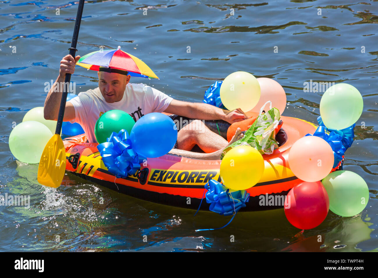 Iford, Dorset, Regno Unito. Il 22 giugno 2019. Il tempo era perfetto, caldo e soleggiato, ancora per Dorset Dinghy giorno con centinaia di gommoni, canotti pneumatici, artigianato, tavole che formano una flottiglia di salpare da ponte Iford giù il fiume Stour a ponte Tuckton. L'evento iniziato nel 2014 come un po' di divertimento, ma ora è diventato un evento annuale la raccolta di fondi per la carità ed il getter più grande di ogni anno. Uomo al divertimento in gommone con palloncini e indossando ombrello hat. Credito: Carolyn Jenkins/Alamy Live News Foto Stock