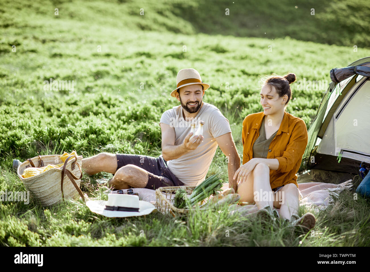 Giovane e allegro giovane avente un picnic presso il campeggio durante un viaggio in alta montagna durante il tramonto Foto Stock