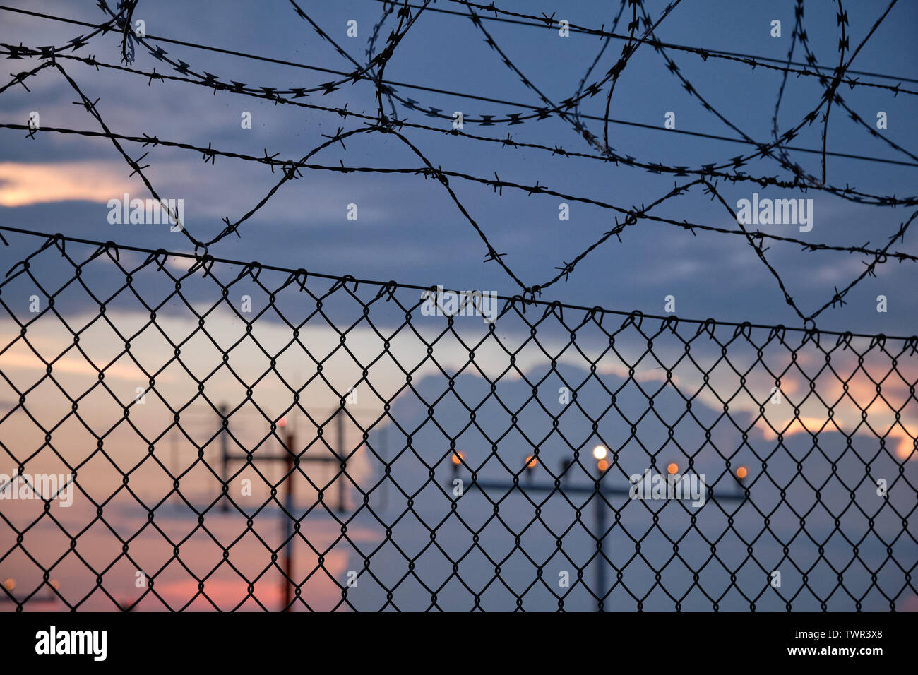 Dettagli di una catena collegamento recinto con filo spinato e nella parte anteriore di un tramonto in un aeroporto Foto Stock