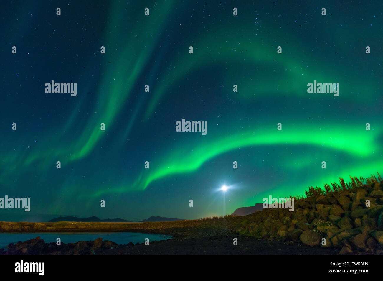 Luna splende con la Northern Lights Visualizzati in Islanda. Colorato cielo di notte, le onde di verde aurora boreale dipinto la notte blu cielo. Foto Stock