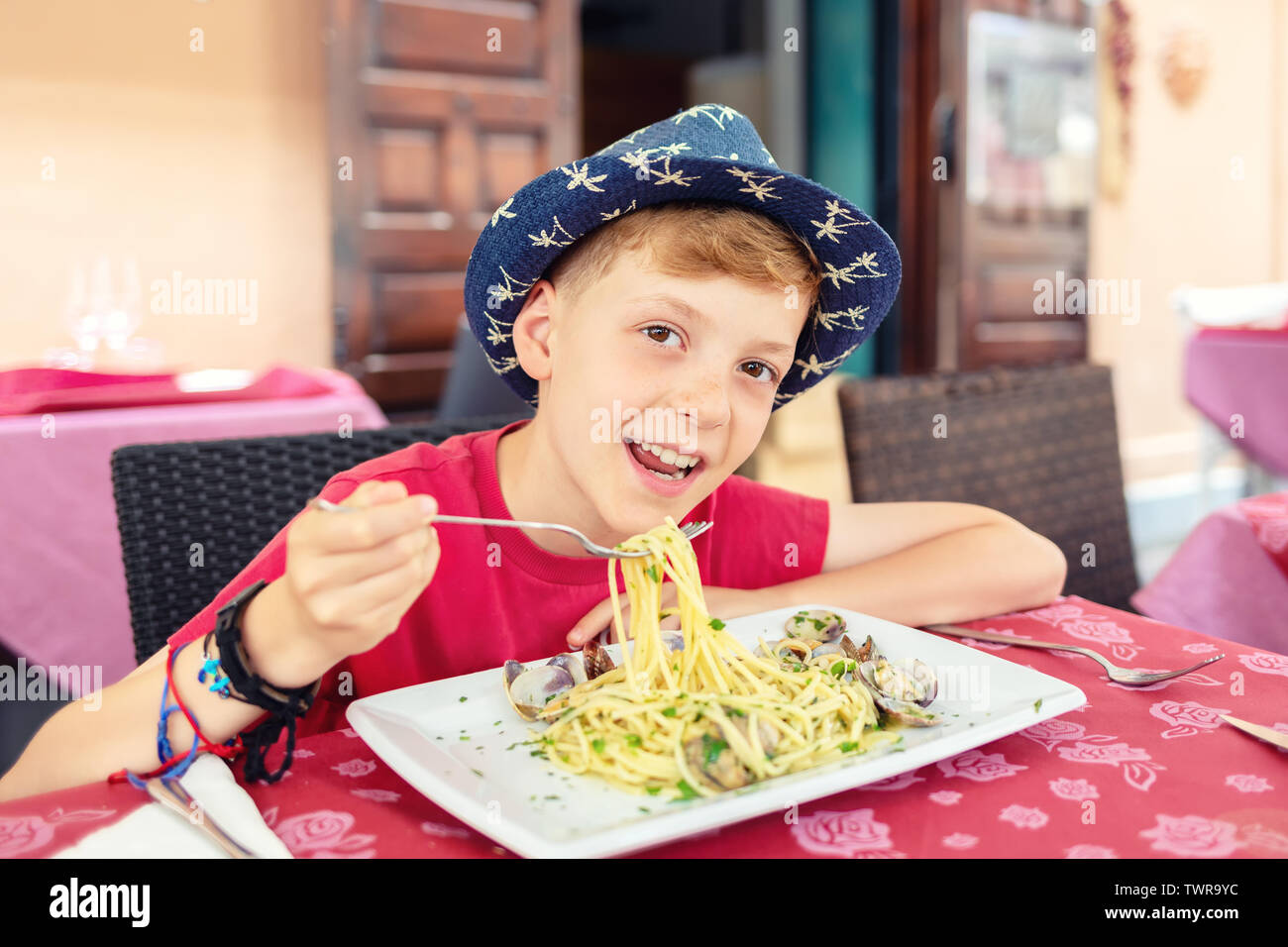Allegro ragazzino mangiare la pasta a base di pesce per pranzo presso il ristorante italiano terrazza Foto Stock