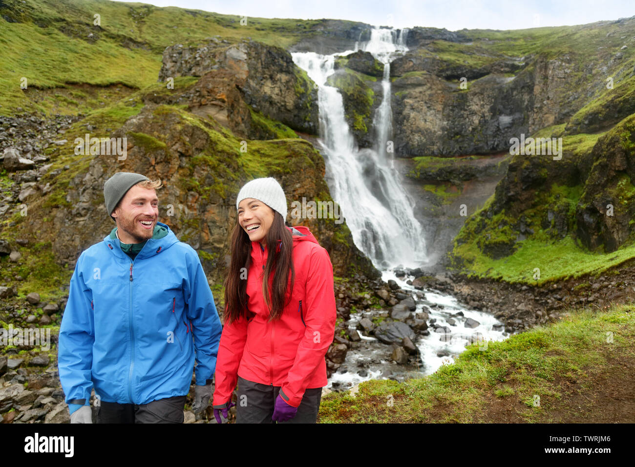 Escursionismo attivo giovane divertenti in cascata in Islanda la natura. La gente parla sorridendo felice in islandese paesaggio turistico in estate. Escursionismo giovane ridendo. Foto Stock