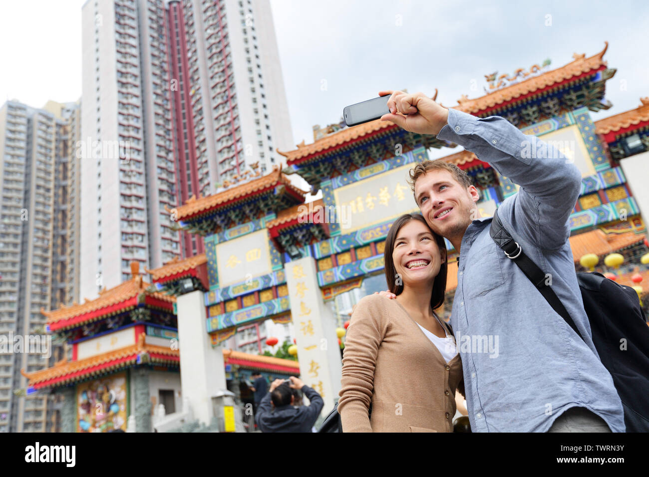 Hong Kong attrazione turistica Wong Tai Sin Temple. I turisti tenendo selfie foto fotografie di famosi Hong Kong landmark. Coppia Romantica visitando e visita il Tempio Taoista. Donna asiatica, uomo caucasico Foto Stock