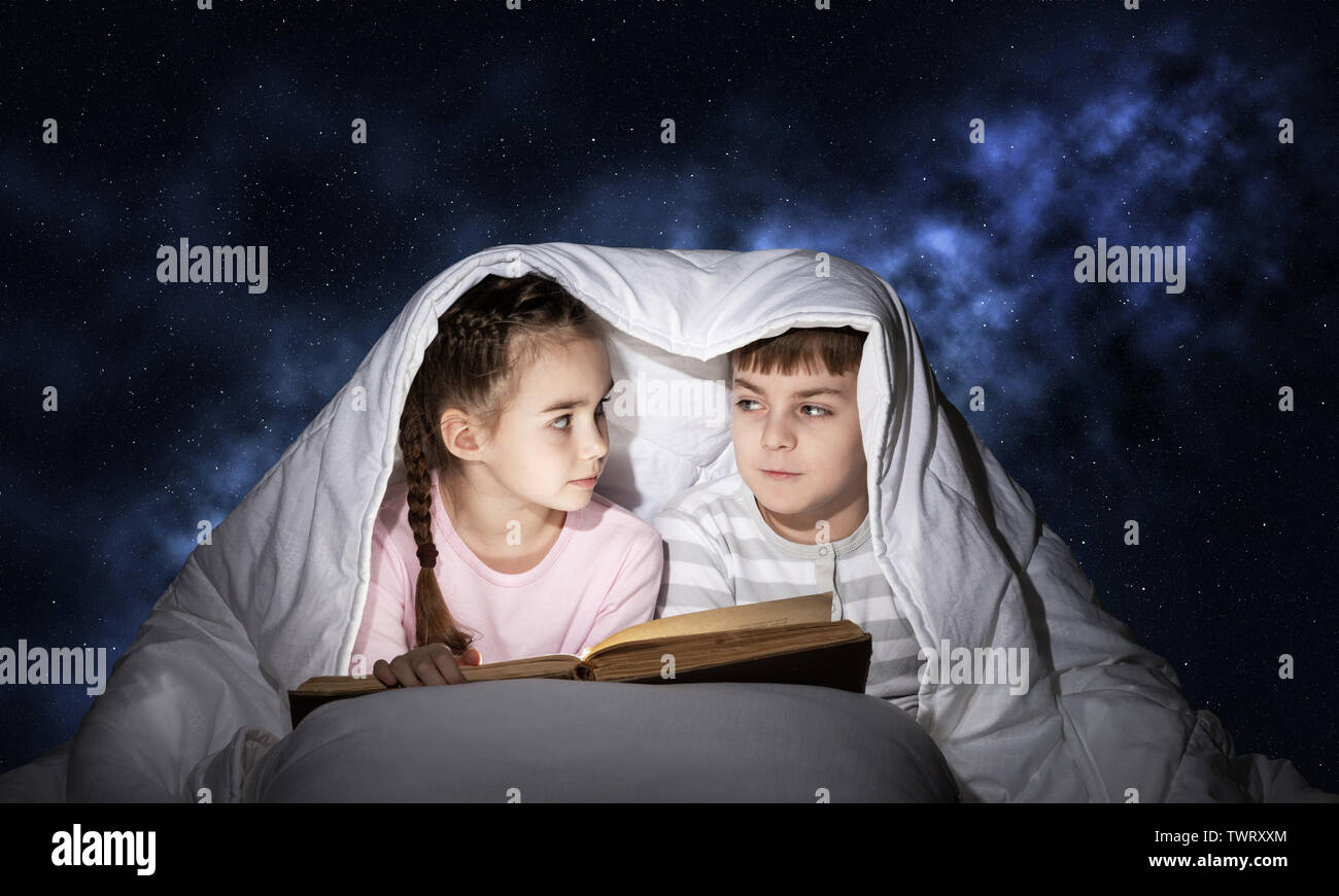 Bambina e ragazzo guardando ogni altro sotto coperta. I bambini la lettura  di storie di magia nel letto prima di andare a dormire. Giovane sorella e  fratello di paja Foto stock -