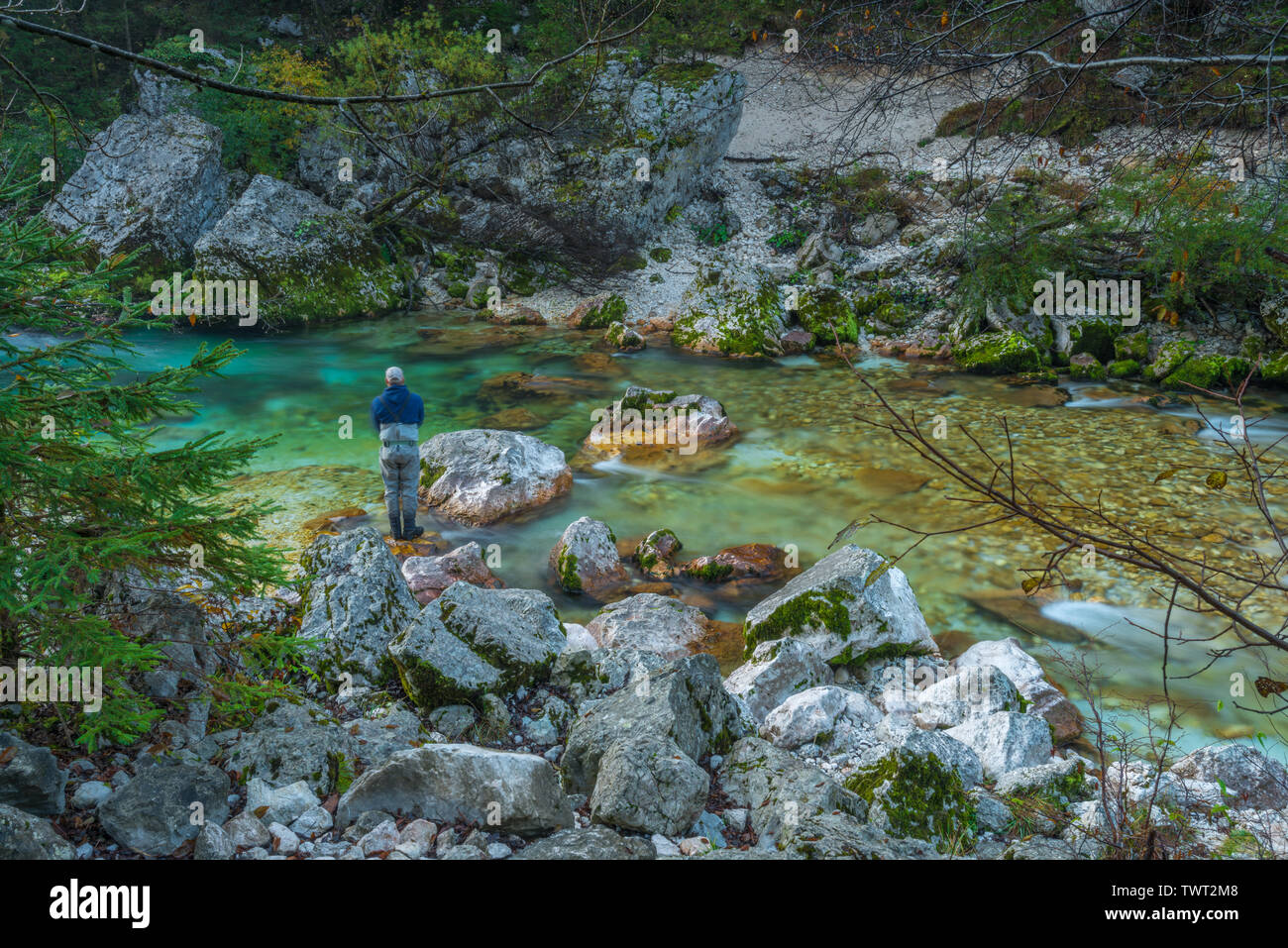 Pescatore solitario la pesca di trote lungo il fiume Soca in Slovenia. La pesca con la mosca in waders per la pesca alla trota lungo immacolate fiume di montagna con rapide. Foto Stock