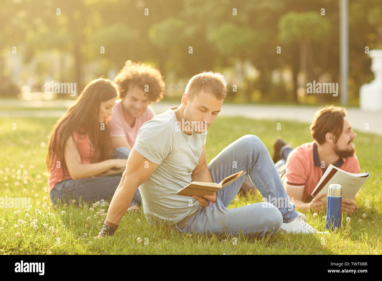 Un gruppo di studenti libri seduto sull'erba al tramonto in un parco della città. Agli studenti di leggere i libri nel parco. Foto Stock