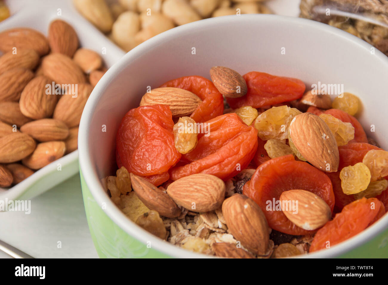 Muesli di fiocchi di cereali con frutta secca, noci nella ciotola verde su bianco tavolo in legno Foto Stock