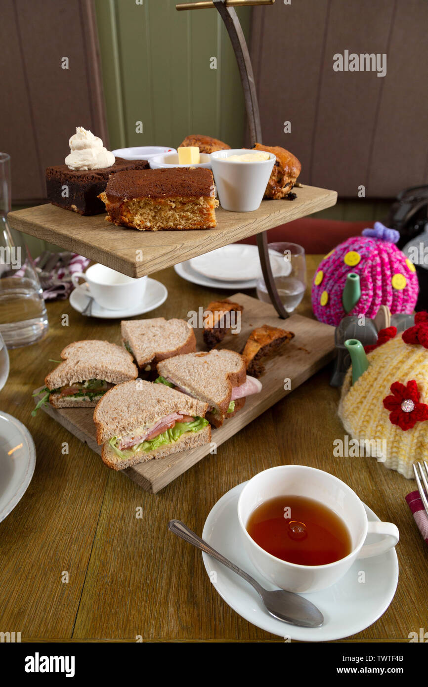 Un rustico di tè pomeridiano servito su una torta in legno stand. Il supporto mani due livelli. Foto Stock