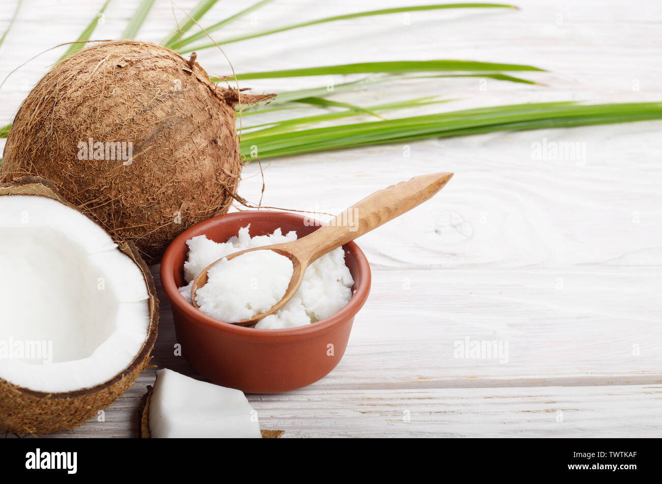 Sfondo di cocco, di guscio di noce di cocco, l'olio nel recipiente di argilla e cucchiaio su bianco tavolo in legno Foto Stock
