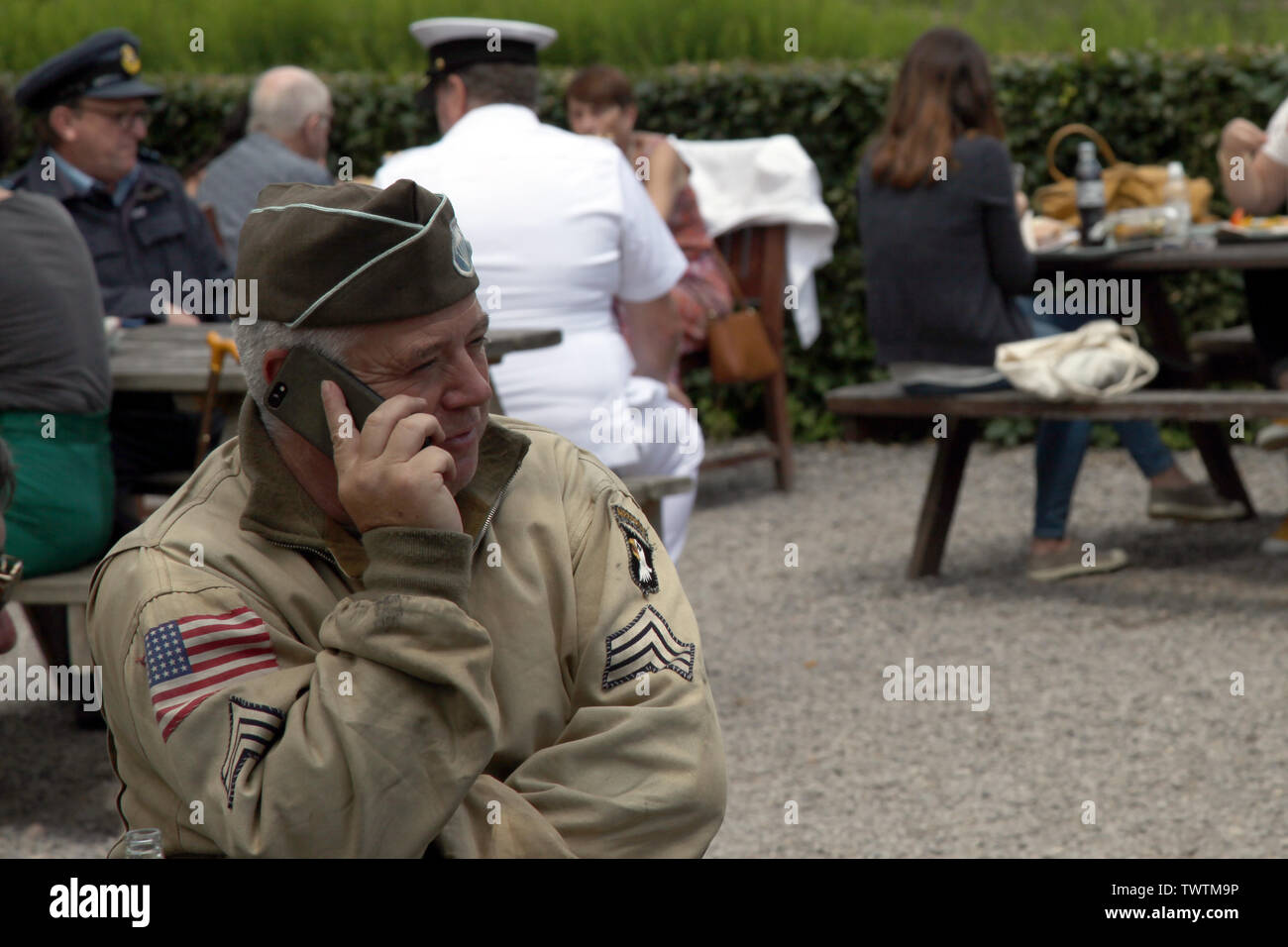Un WW2 rievocazione storica di un esercito americano sergente di 101st Airborne in camicia di Ike e tappo di guarnigione si rilassa su un giorno moderno telefono cellulare Foto Stock