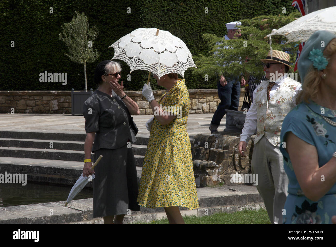Edenbridge, Kent, Regno Unito - onorevoli avente una conversazione che indossa fiorito di 1940s fashion con pizzo bianco ombrellone nella luce del sole durante il giorno Foto Stock
