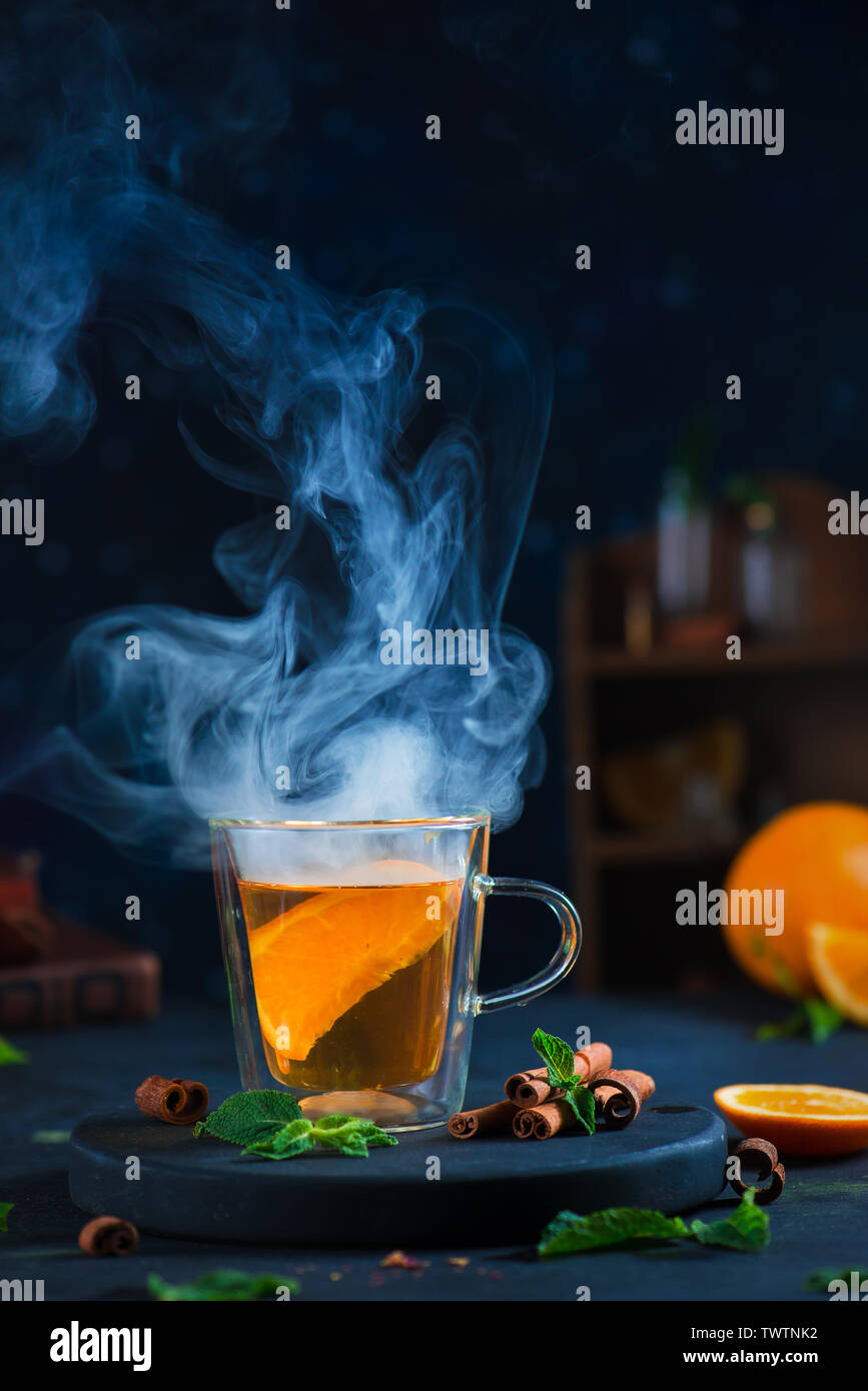 Doppia parete in vetro con tazza di tè di agrumi, cannella e foglie di menta. Vapore nel buio fotografia alimentare con copia spazio. Foto Stock