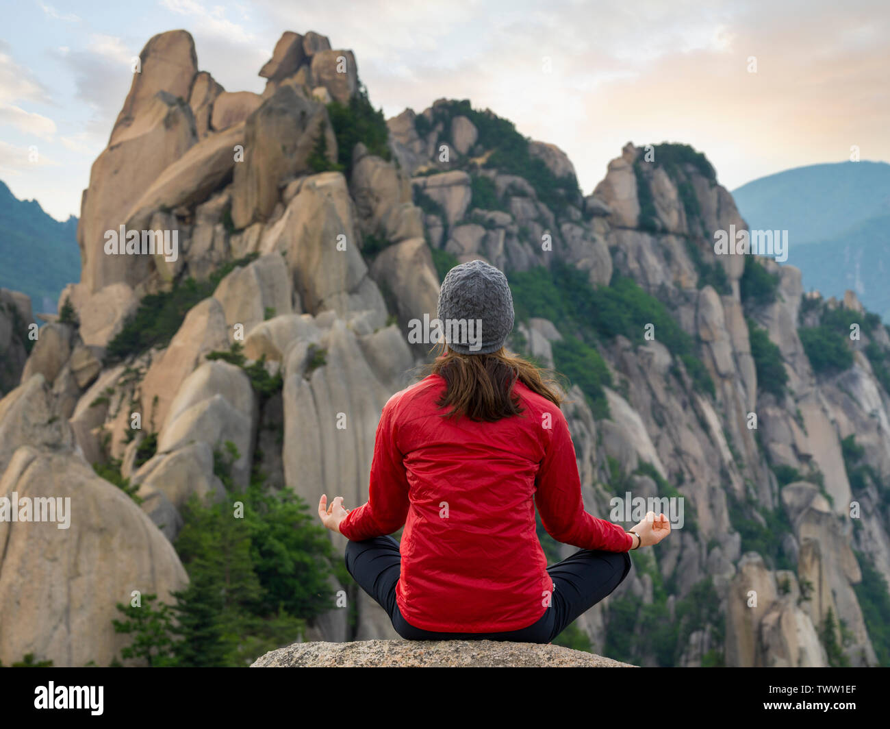 Con le gambe incrociate giovani escursionista meditando sulla sommità del monte Ulsan in Corea del Sud durante il tramonto Foto Stock