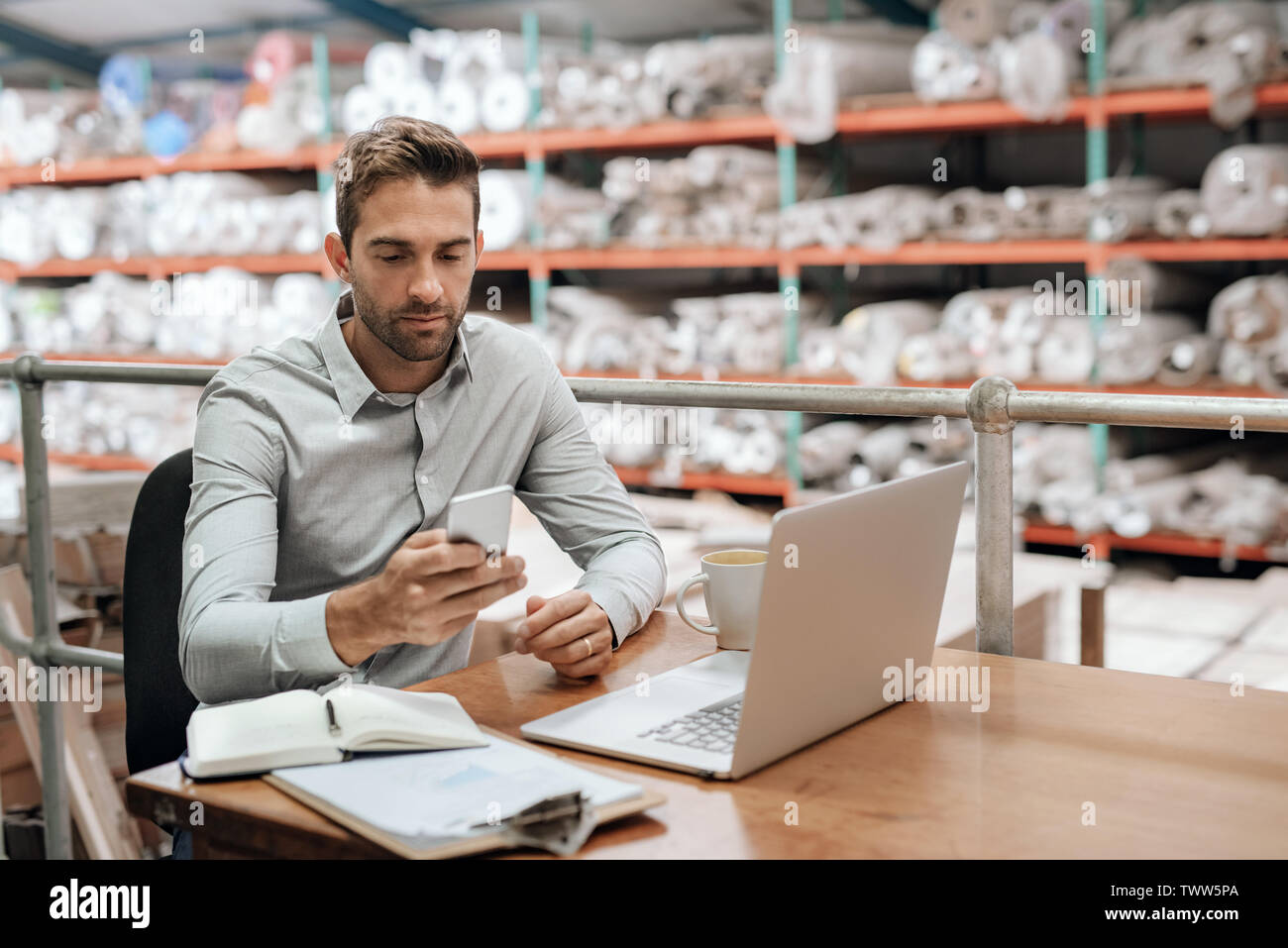 Responsabile di Magazzino controllando il suo cellulare mentre si lavora nel suo ufficio Foto Stock