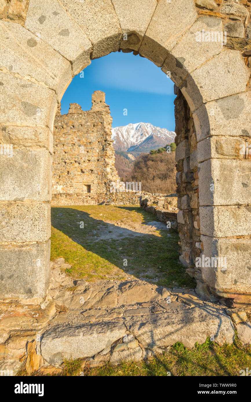 Montagne dalle vette innevate vista attraverso arco in pietra, resti del castello medievale a Cimbergo, Val Camonica. Vecchia Fortezza nelle montagne dell'Italia. Foto Stock