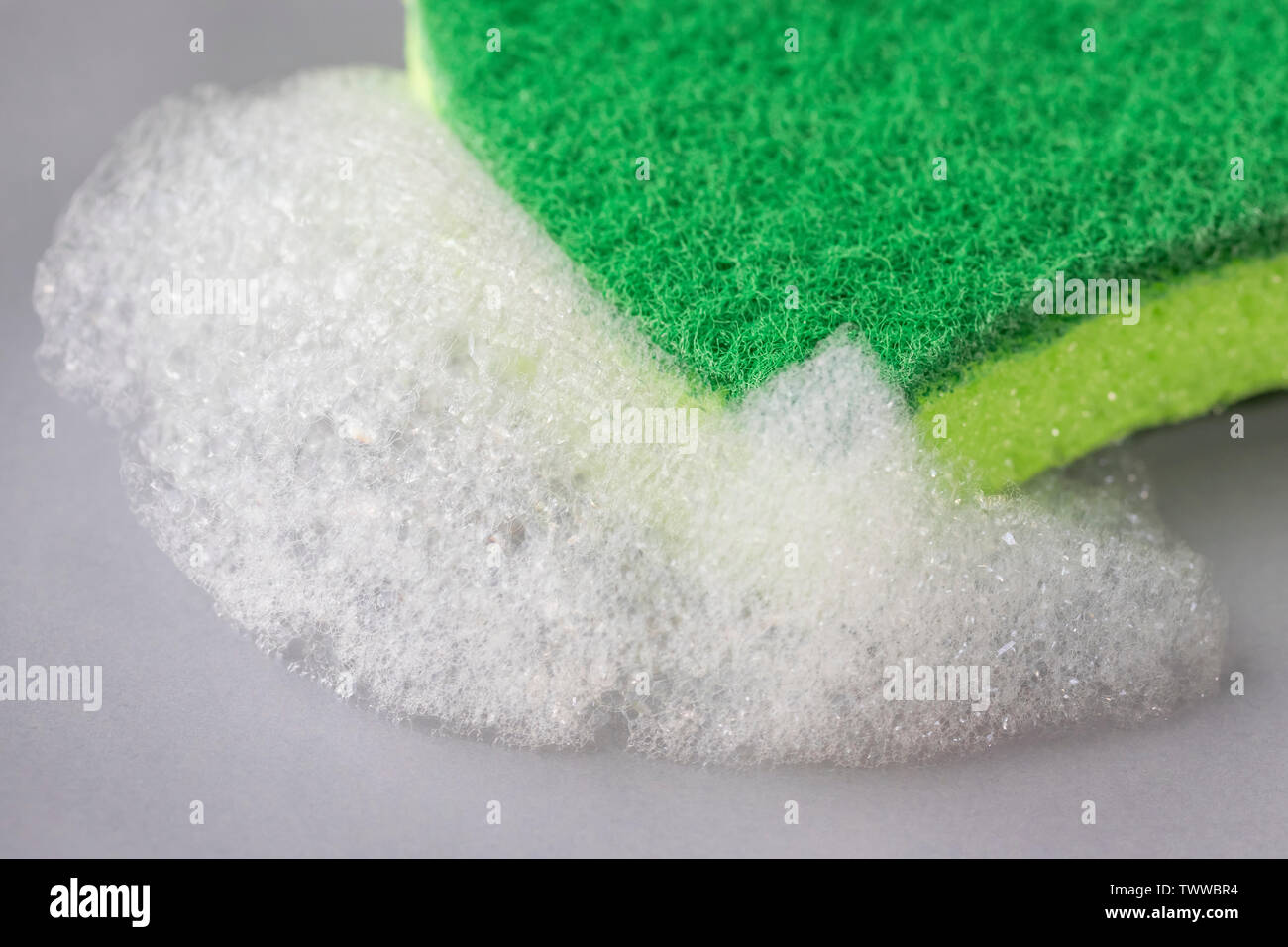 Cucina spugna verde con detergente in schiuma su una lastra grigia. Il lavaggio e la pulizia delle stoviglie e utensili domestici Foto Stock