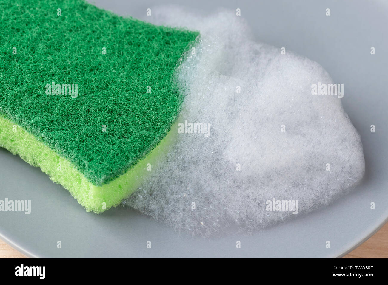 Cucina spugna verde con detergente in schiuma su una lastra grigia. Il lavaggio e la pulizia delle stoviglie e utensili domestici Foto Stock