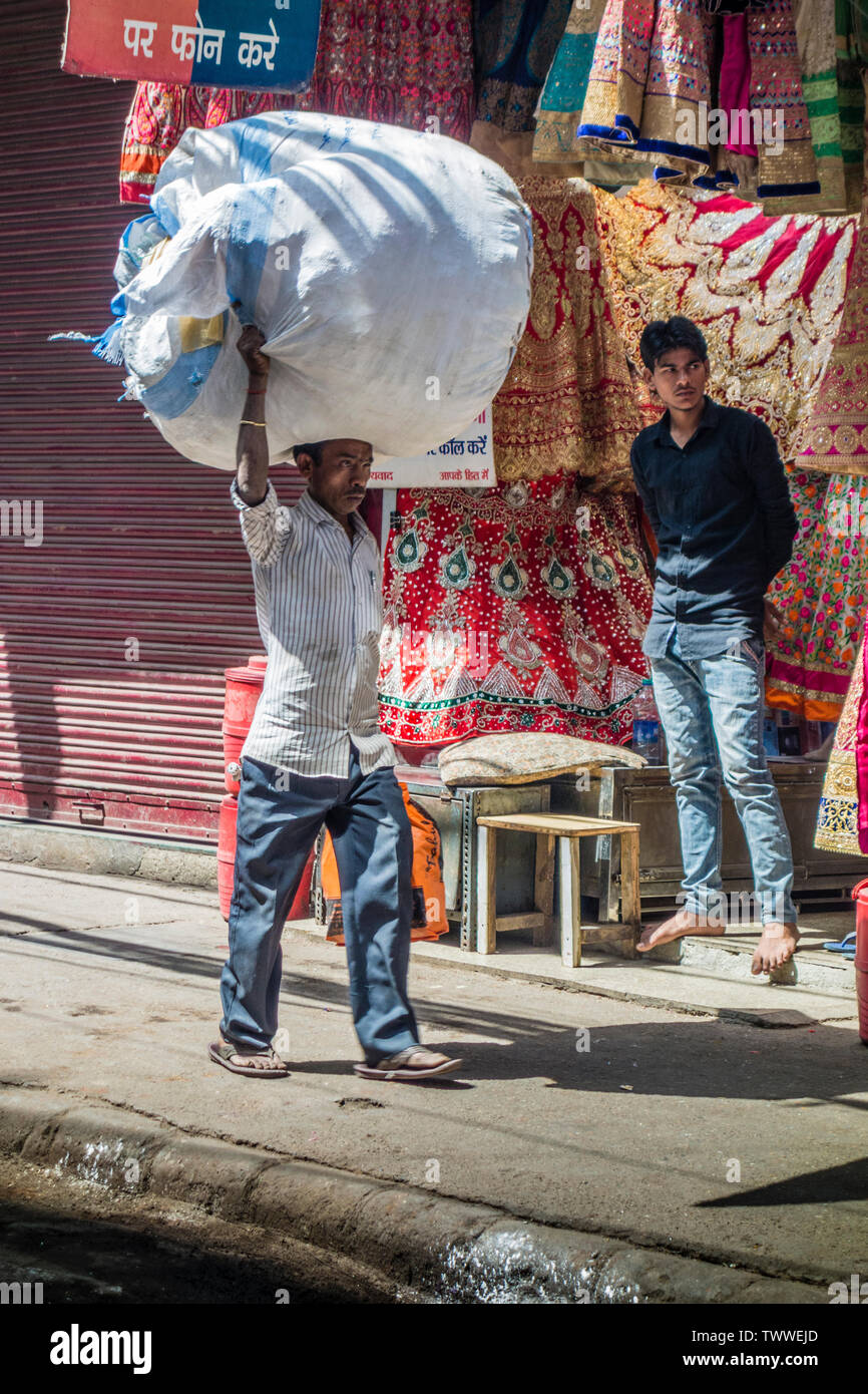 Uomo che porta un enorme fardello sul suo capo su un business street nella Vecchia Delhi, New Delhi, India Foto Stock