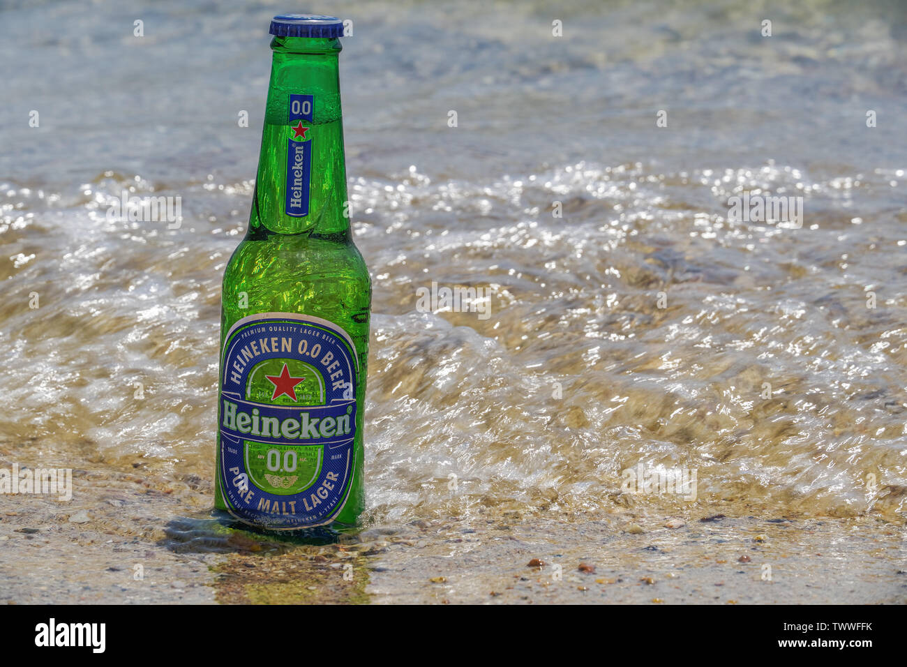 Heineken alcol zero bottiglia di birra sulla sabbia dal mare. Sunny View di analcolici birra chiara su un 33cl bottiglia di vetro parzialmente sommerso sulla spiaggia sabbiosa. Foto Stock