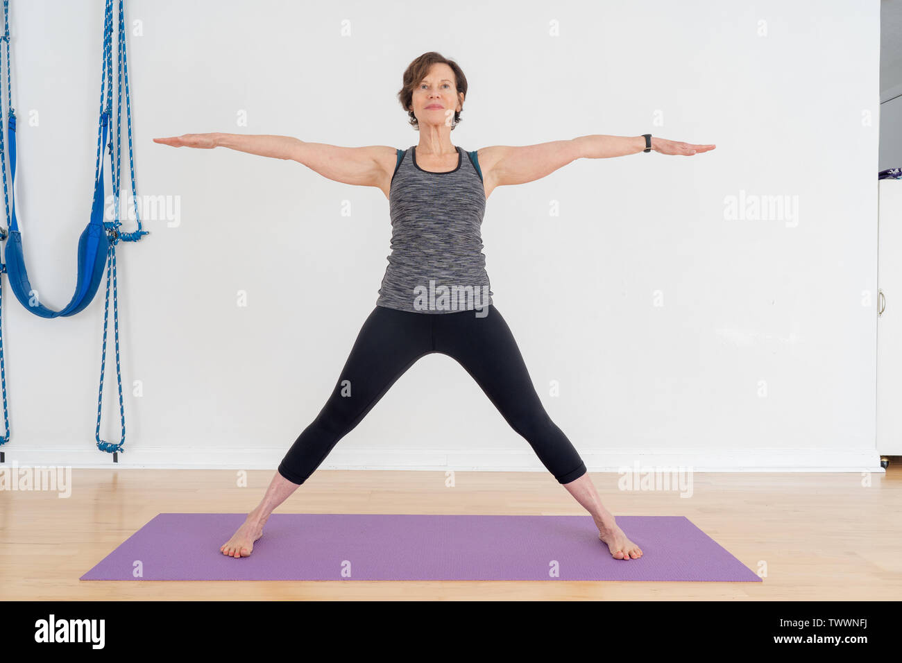 Un vecchio di 70 anni donna istruttore yoga nel suo studio mostra posizione Yoga chiamato Virabhadra posa è anche conosciuto come il guerriero pongono Foto Stock
