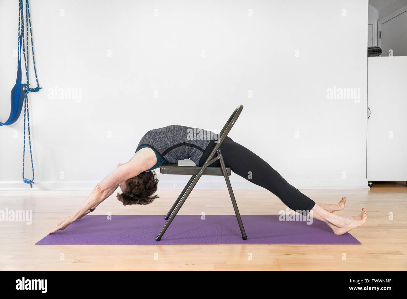 Un vecchio di 70 anni donna istruttore yoga nel suo studio mostra Iyengar Yoga Backbend sedia Foto Stock