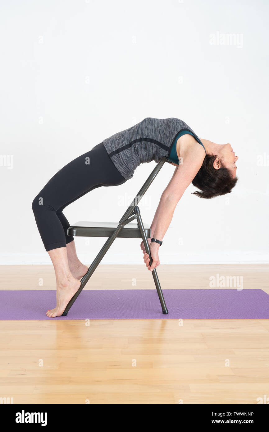 Un vecchio di 70 anni donna istruttore yoga nel suo studio mostra Iyengar Yoga Backbend sedia Foto Stock