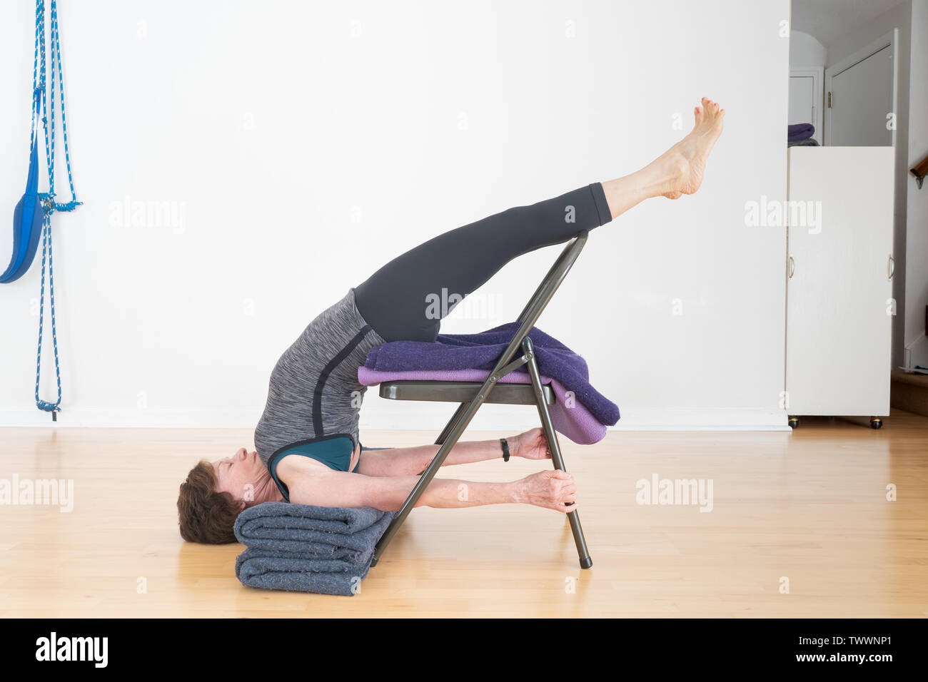 Un vecchio di 70 anni donna istruttore yoga nel suo studio mostra Iyengar Yoga Backbend sedia Foto Stock