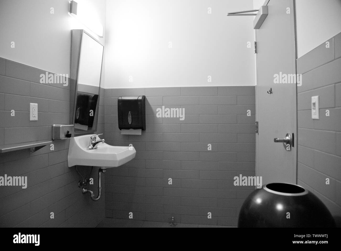 Foto in bianco e nero di uno specchio, asciugacapelli a mano, cambiare tavolo e lavello in un bagno pubblico Foto Stock