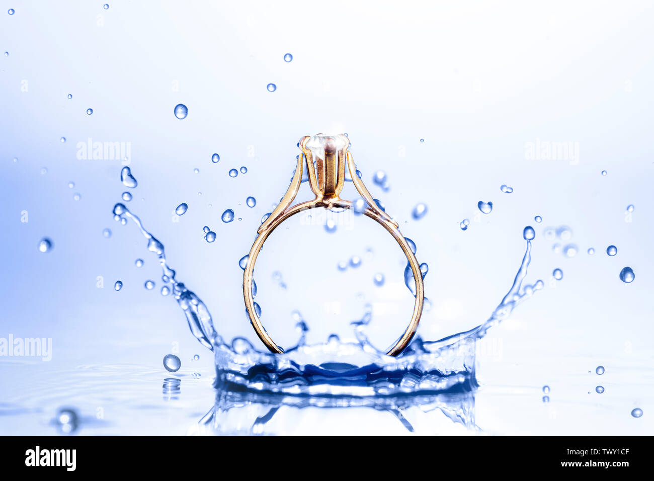 Splendido oro diamanti anello macro closeup schizzi su acqua blu Foto Stock