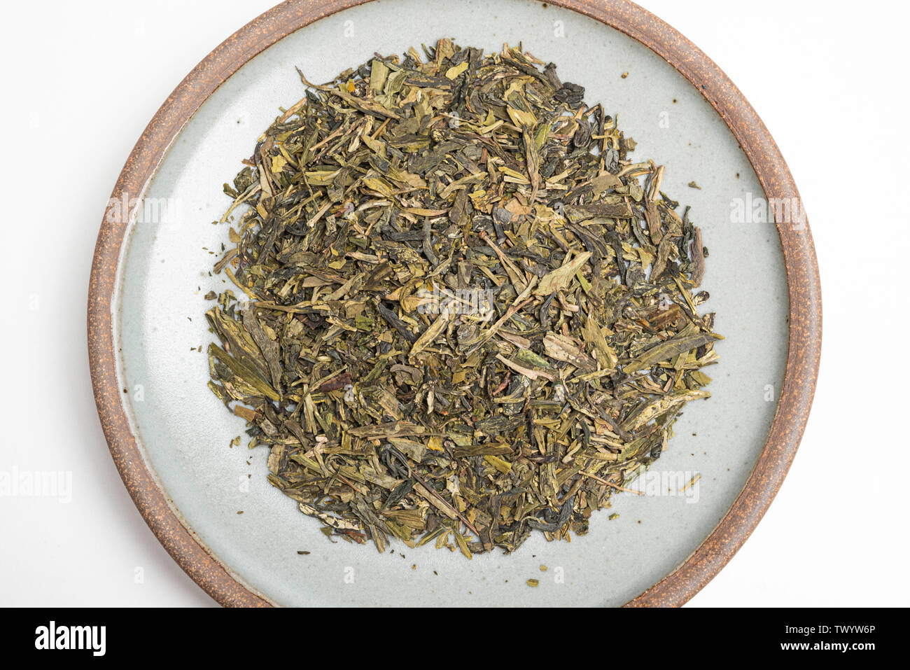 Un prodotto di studio shot di un mazzetto di cinesi secchi di foglie di tè verde sul round emerald porcellanato impostato su sfondo bianco. Foto Stock