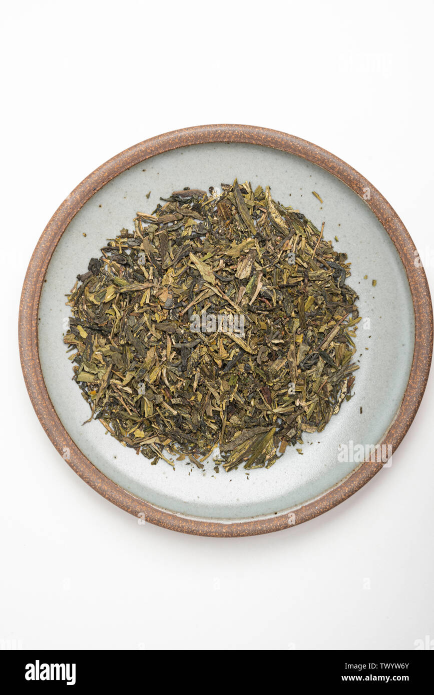 Un prodotto di studio shot di un mazzetto di cinesi secchi di foglie di tè verde sul round emerald porcellanato impostato su sfondo bianco. Foto Stock